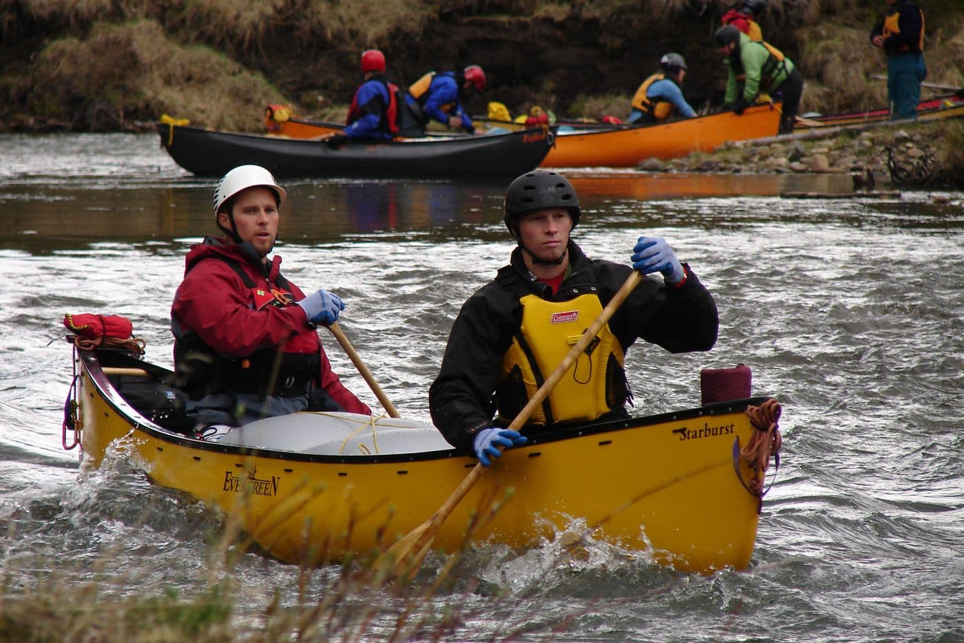 A lady and a dog sitting in a tent overlooking the water.