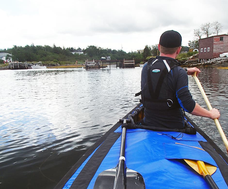 A lady and a dog sitting in a tent overlooking the water.