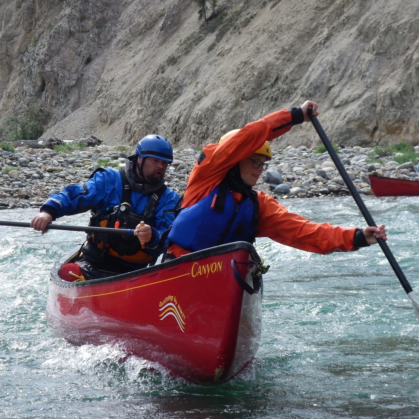 A lady and a dog sitting in a tent overlooking the water.